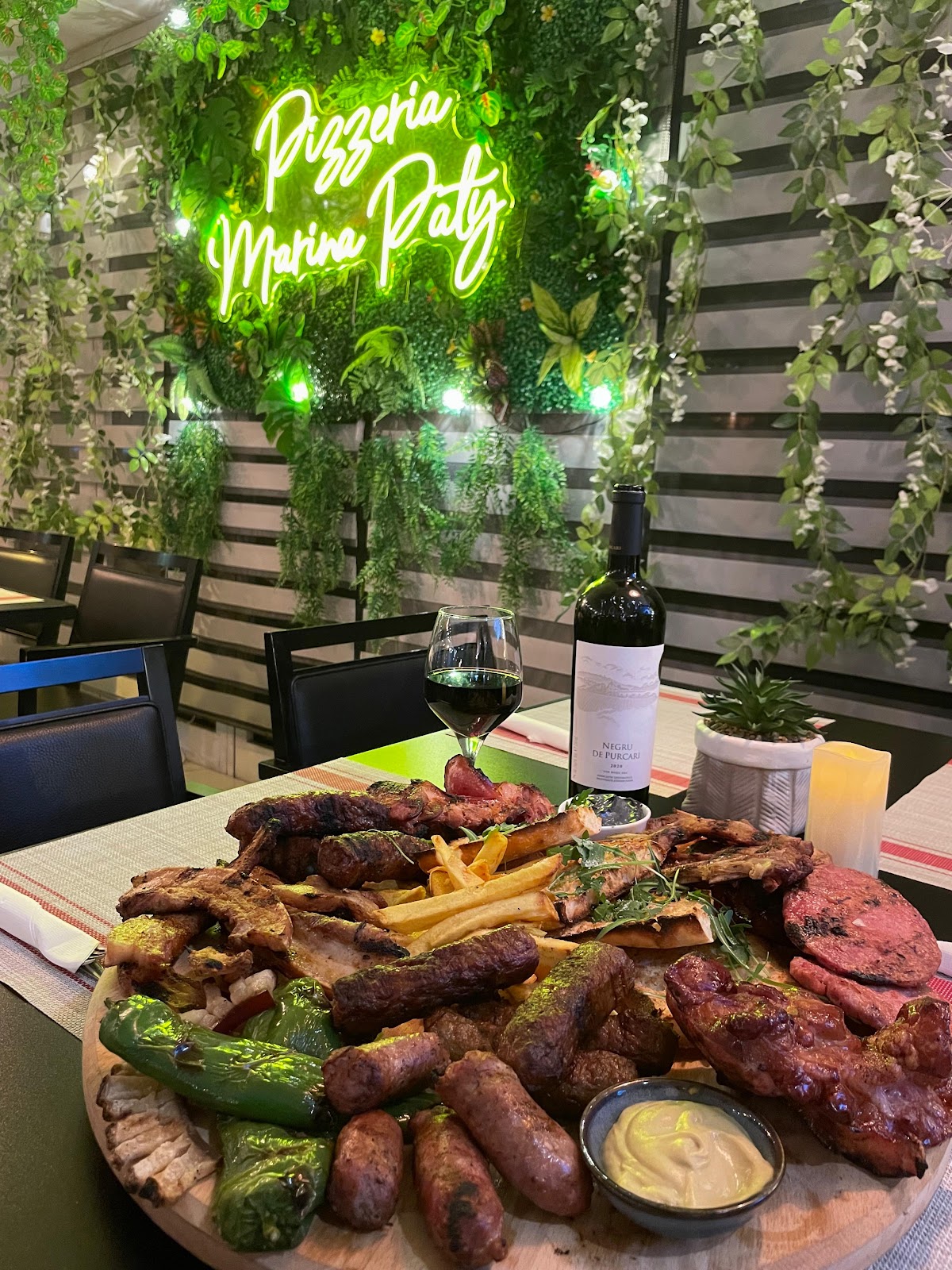 Tabla de carnes y mici rumanos servida bajo el neón Pizzería Marina Paty